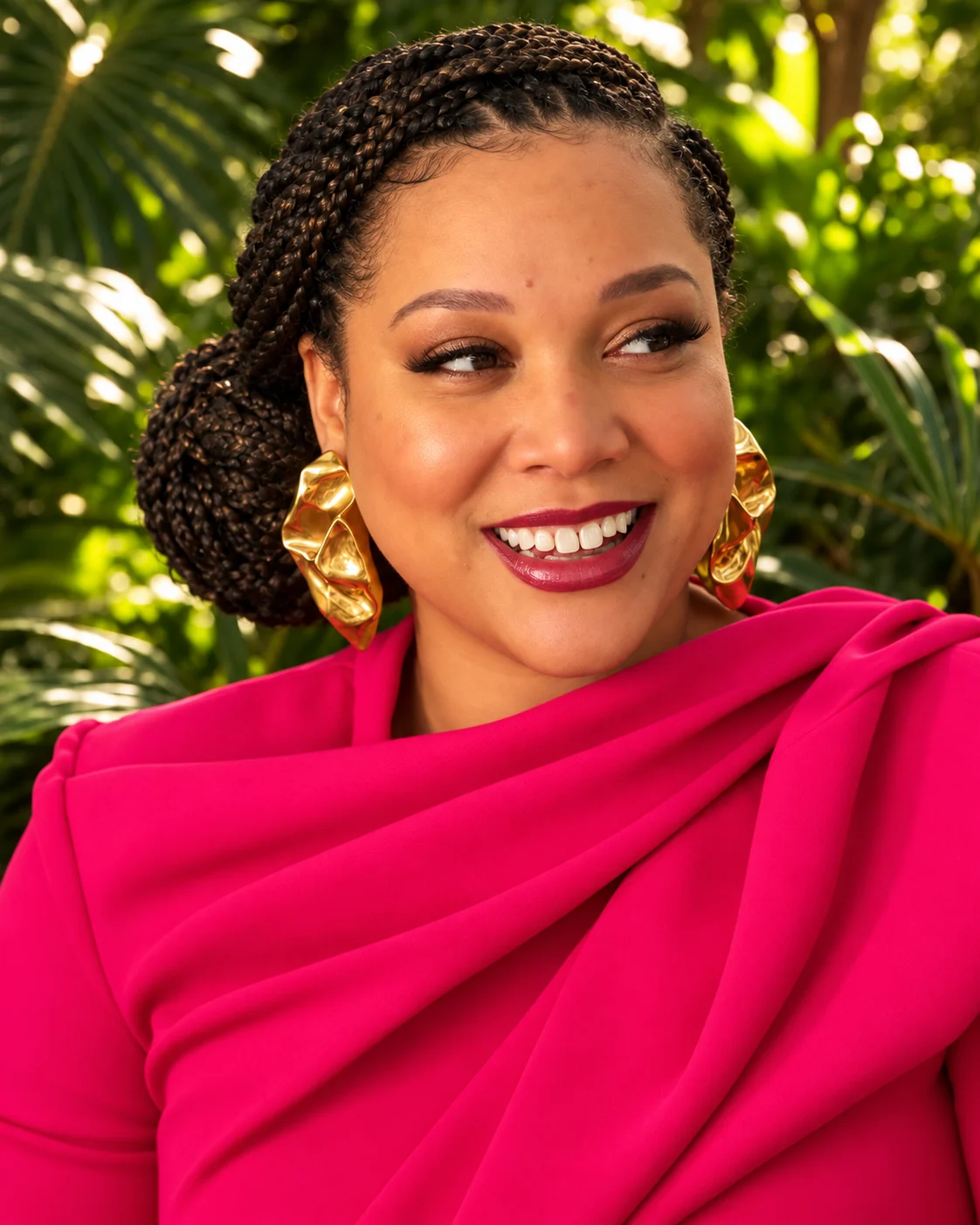 Portrait of K.B. Keene, founder of the Pretty Is a Practice Initiative, smiling in a draped pink top and sculptural gold earrings.